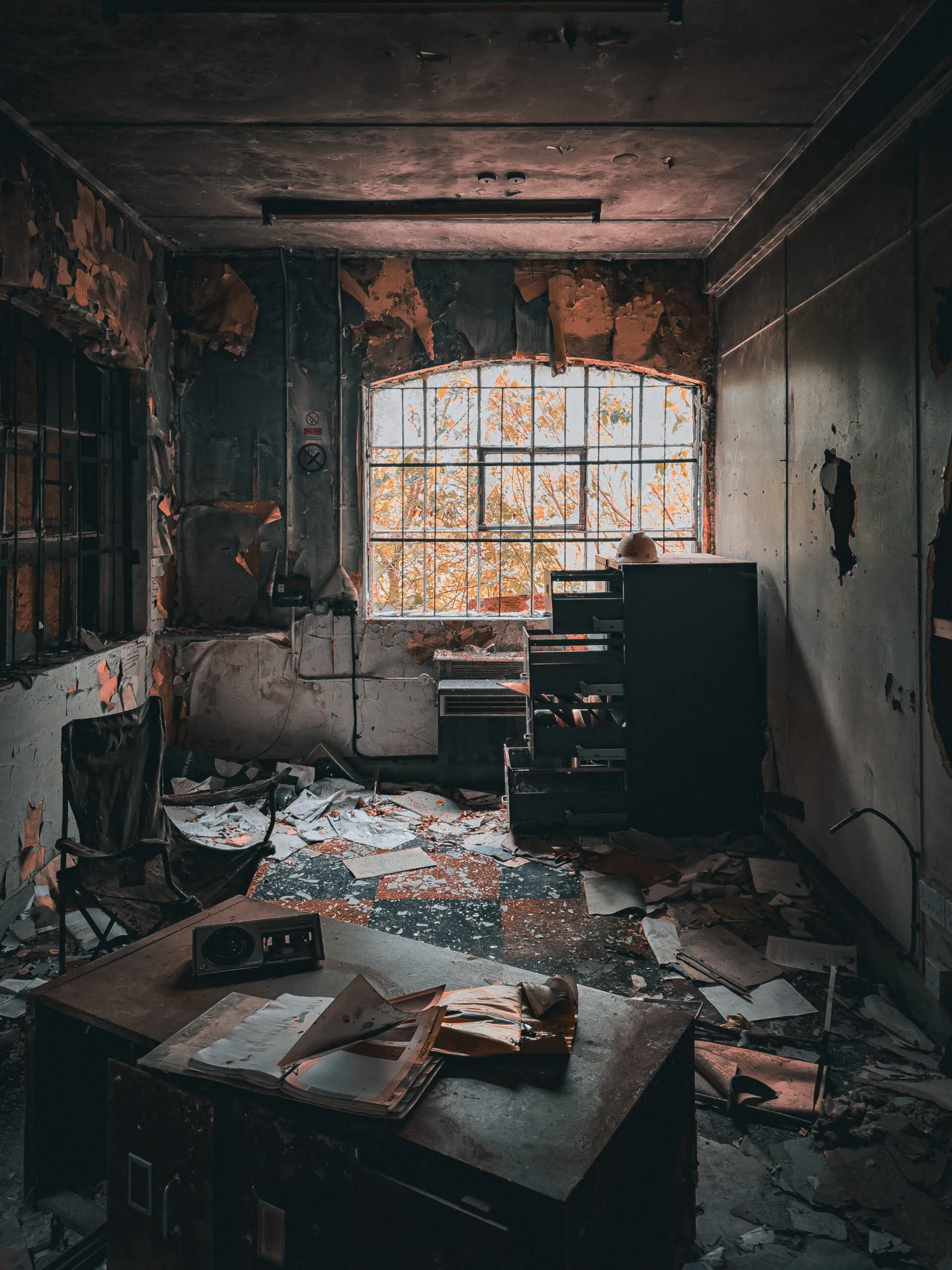 An abandoned works office, papers spread across a desk and spilling from an open filing cabinet, autumn leaves outside the arched window
