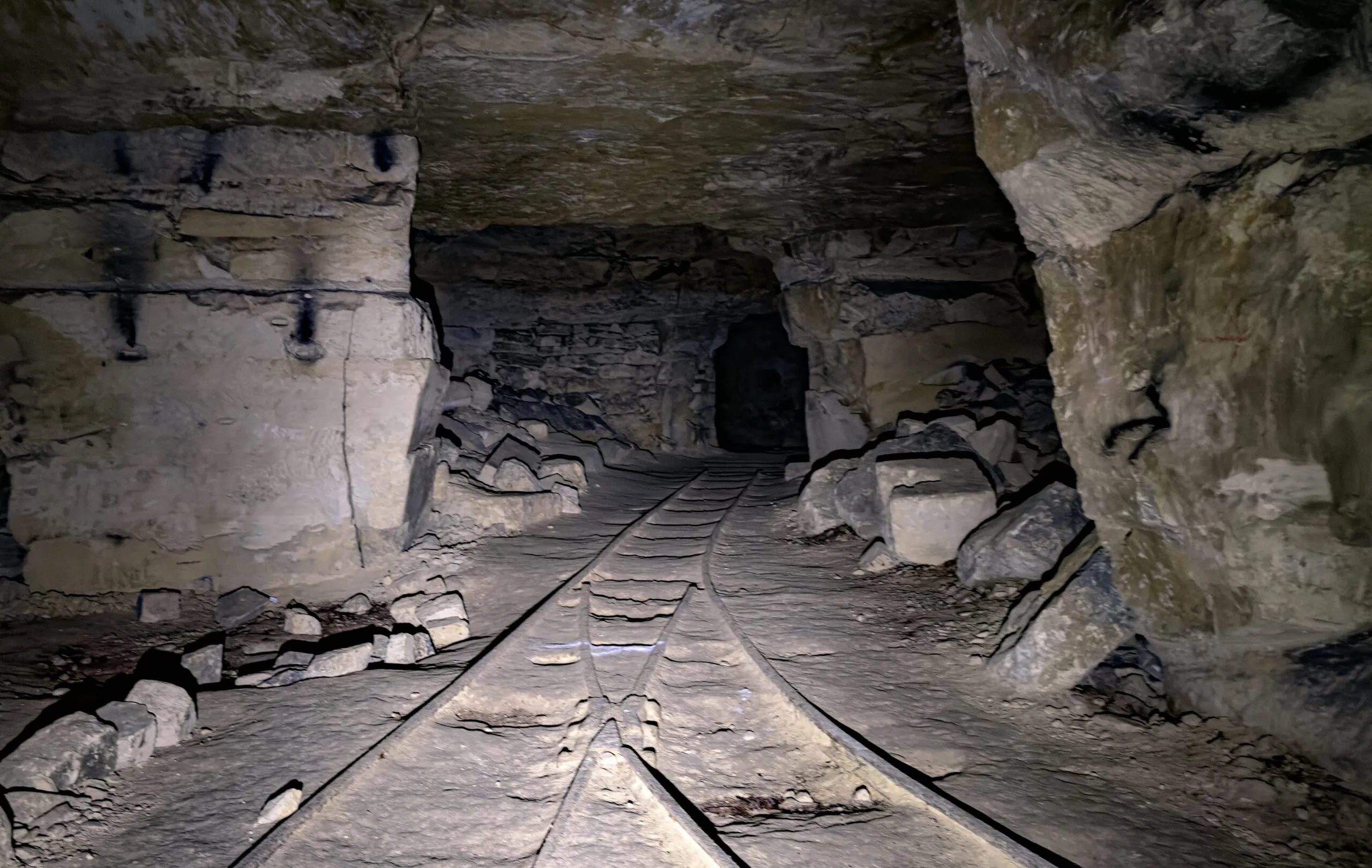Tramway rails running away down a stone-cut passage and converging at a low opening in the distance
