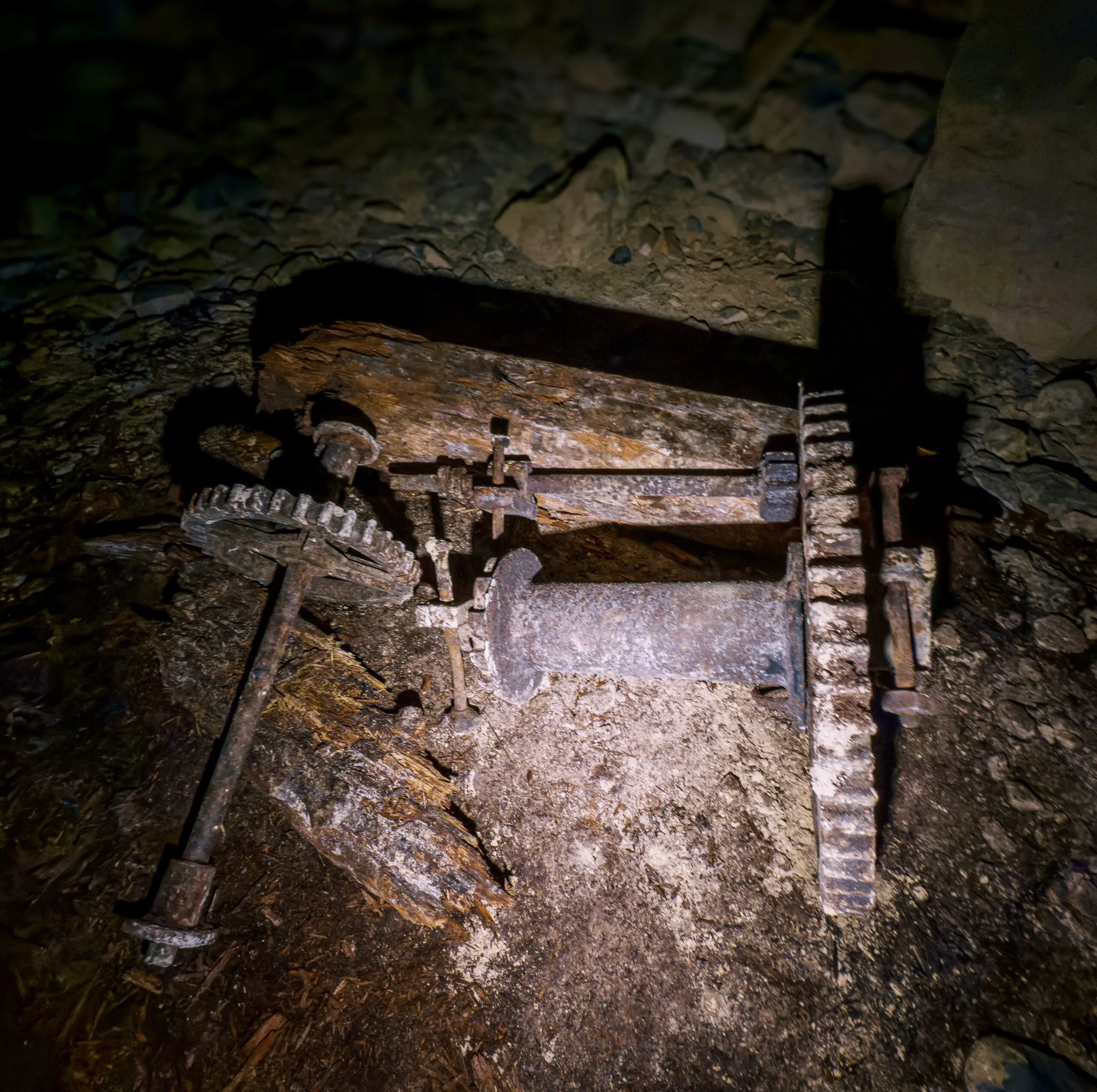 Rusted winch gearing left underground, two toothed gear wheels still mounted on a decaying timber bed