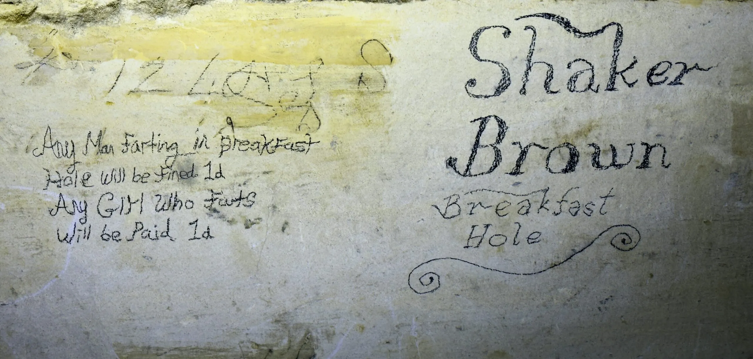 Miners' writing on a pale stone wall reading 'Shaker Brown Breakfast Hole', with a joke below about fines for breaking wind